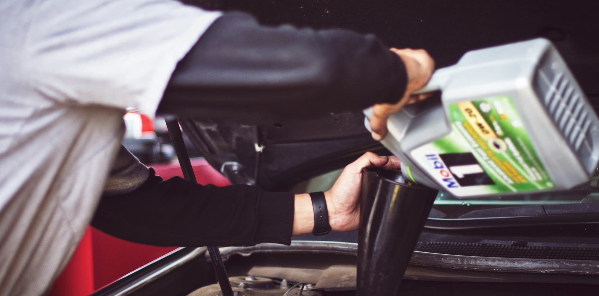 man refilling motor oil on car engine bay