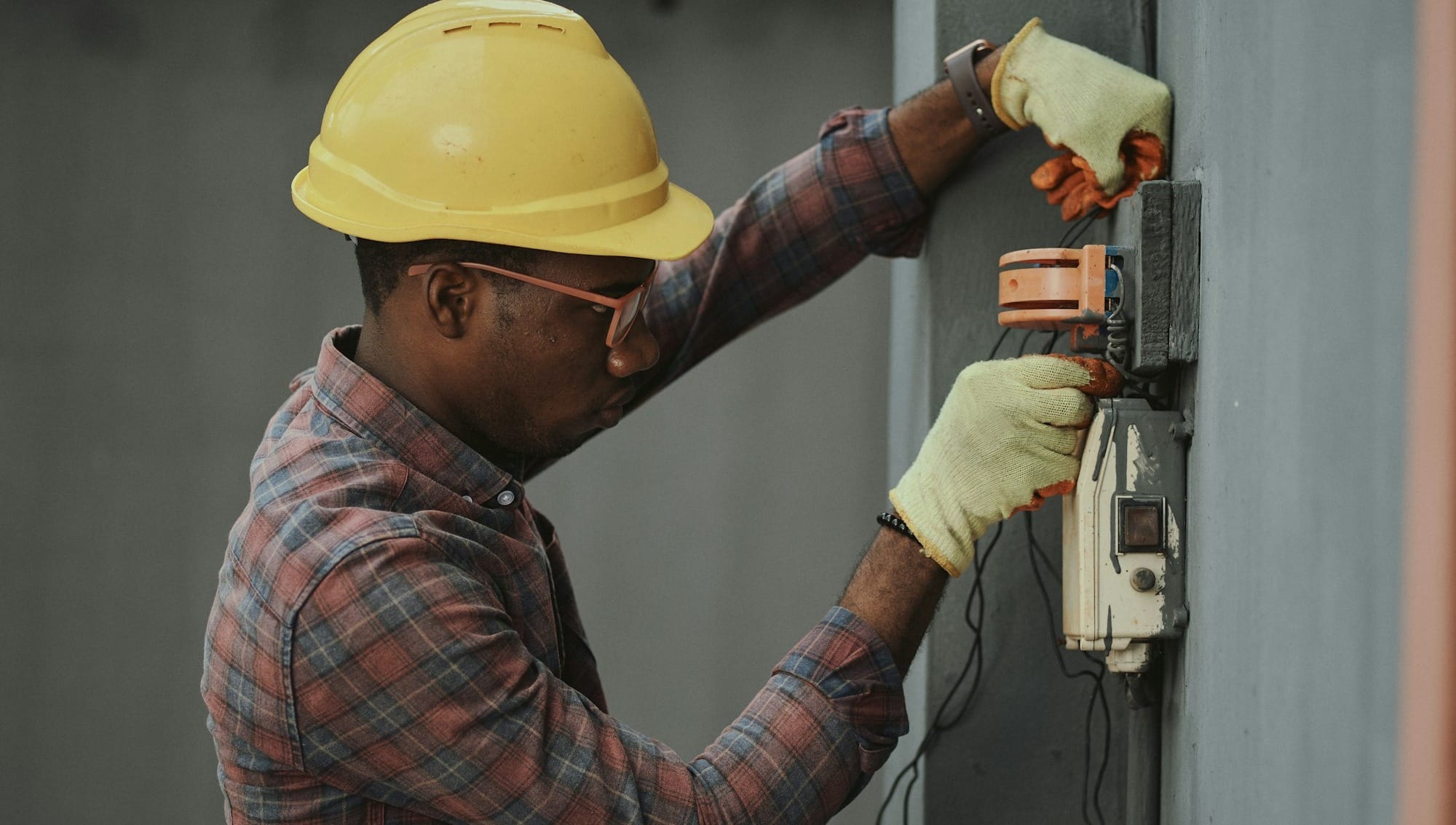 man in brown and white plaid dress shirt and yellow hard hat holding black and orange