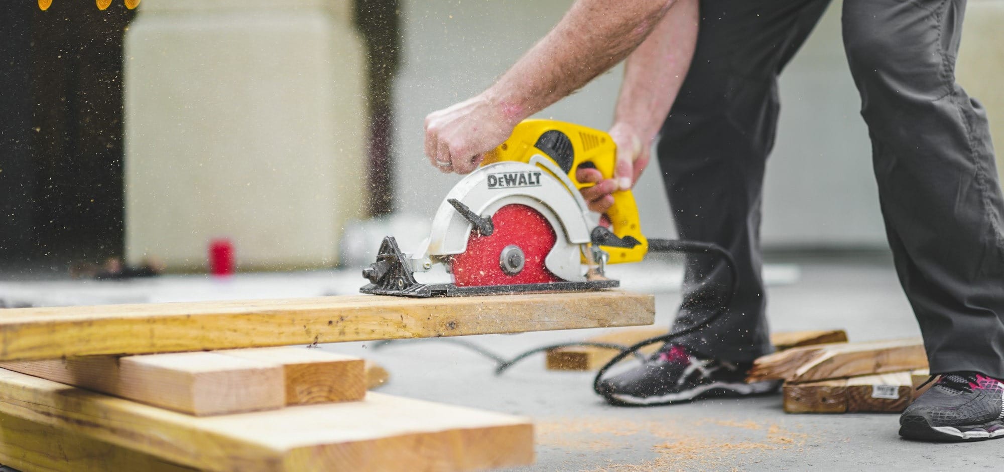 man in black sweatpants using DEWALT circular saw and cutting a wood plank